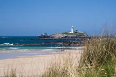 a sandy beach with a lighthouse in the ocean at Countryside Cabin in Private Setting in Redruth