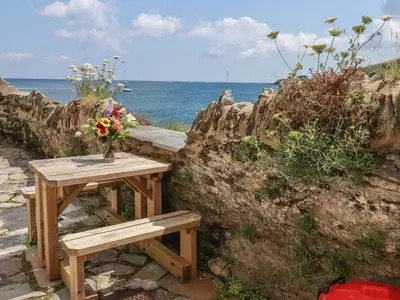 a wooden table and bench with a vase of flowers at Chy Rani in Portmellon