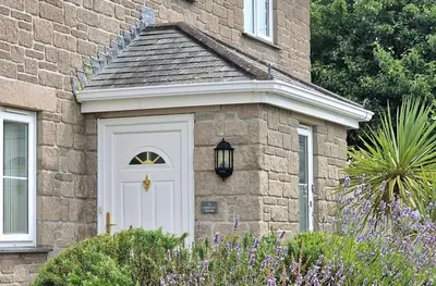 a brick house with a white door and flowers at Chestnut House in Saint Columb Minor