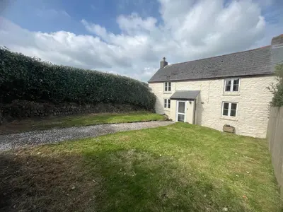 a white house with a stone wall next to a yard at 1 Carnebone Cottages in Porkellis