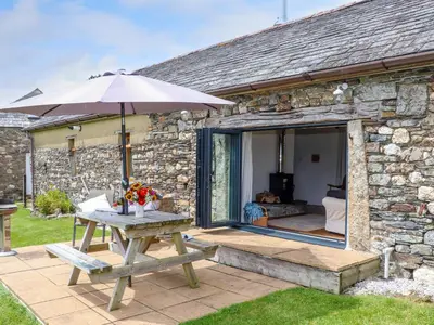 a picnic table with an umbrella next to a stone cottage at Skiber Long in Callington