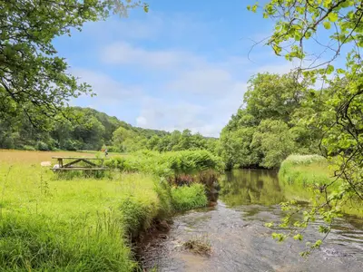 a river in a field with a bridge and trees at Skiber Long in Callington