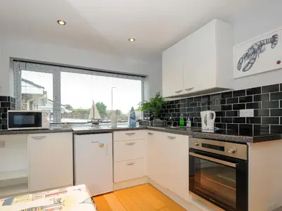 a kitchen with white cabinets and black tile on the wall at Coastal Haven in Bude