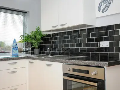 a kitchen with white cabinets and black tile on the wall at Coastal Haven in Bude