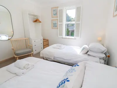 a bedroom with two beds and a chair and a window at Mariners Watch in St Ives