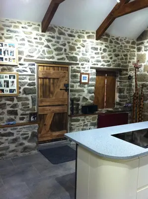 a kitchen with a stone wall and a wooden door at Anvil The Old Smithey in Saint Erth