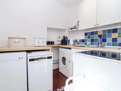 a kitchen with white cabinets and a washer and dryer at The Dairy in Liskeard
