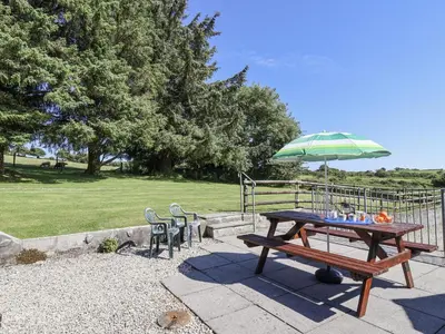 a picnic table with a green umbrella and chairs at The Byre in Liskeard