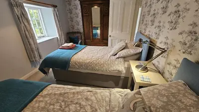 a bedroom with two beds and a desk with a lamp at Glebe Barn in Ruan Lanihorne