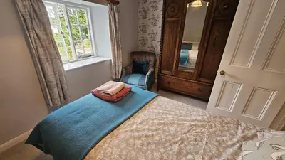a bedroom with a bed and a chair and a window at Glebe Barn in Ruan Lanihorne