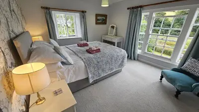 a bedroom with a bed and two windows at Glebe Barn in Ruan Lanihorne