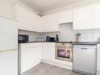 a white kitchen with white cabinets and a dishwasher at Mor Kernow in St Ives