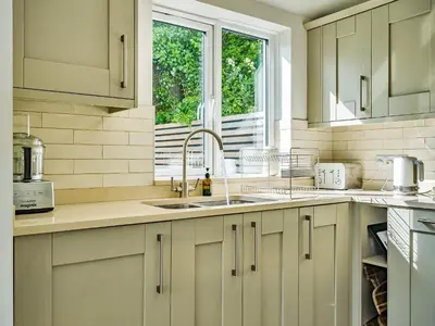 a kitchen with white cabinets and a sink and a window at Fairwinds in Portreath