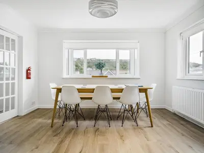 a white dining room with a wooden table and white chairs at Fairwinds in Portreath
