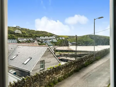 a house sitting next to a stone wall next to a street at Fairwinds in Portreath