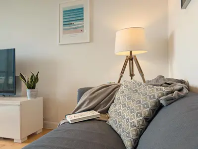 a pillow on a couch with a lamp and a book at Modern Apartment By The Beach in Newquay