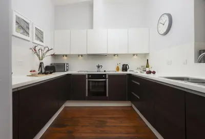 a kitchen with white cabinets and a clock on the wall at The Old Carriage Works in Lostwithiel