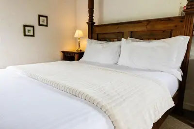 a large white bed with a wooden headboard and white pillows at Bligh - Treworgie Barton Cottages in Bude