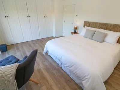 a bedroom with a large white bed and a chair at 2 The Dunes in Falmouth
