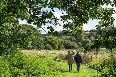 a man and woman walking through a field at Manor Cottage at Cusgarne Manor, romantic, dog-friendly in Cusgarne