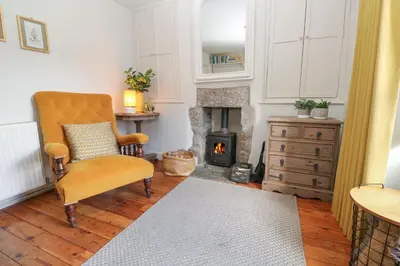 a living room with a chair and a fireplace at Apple Tree Cottage in Helston