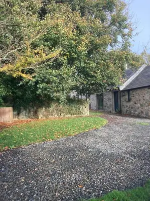 a stone house with a tree next to a driveway at Little Barn in Bodmin
