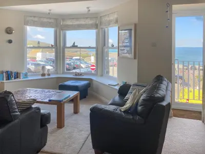 a living room with couches and a table and windows at Ocean Breezes in St Ives