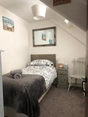 a bedroom with a bed and a mirror and a chair at Guillemot Holiday Flat in Looe