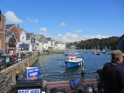 a man sitting on a bench watching a boat in a river at Gunnado in St Austell
