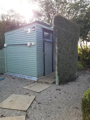 a garage with a door next to a hedge at The Shepherd Hut in Carleen