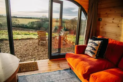 a living room with a couch and a large window at The Palm at OLJU Lodges in Ponsanooth