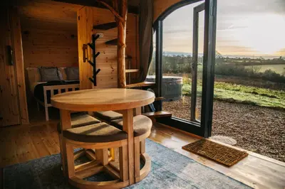 a wooden cabin with a table and a window at The Palm at OLJU Lodges in Ponsanooth