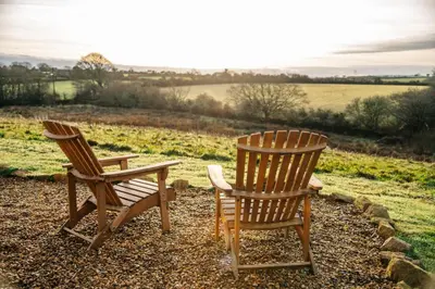 two wooden chairs and a table in a field at The Palm at OLJU Lodges in Ponsanooth