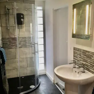 a bathroom with a glass shower and a sink at Wildly Romantic Cliff Top Apartment in Porthleven