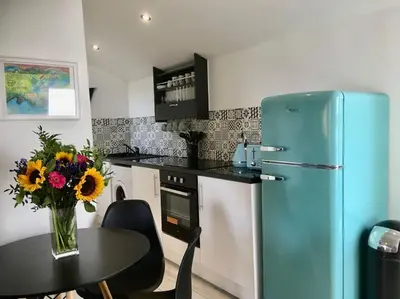 a kitchen with a blue refrigerator and a table with flowers at Wildly Romantic Cliff Top Apartment in Porthleven