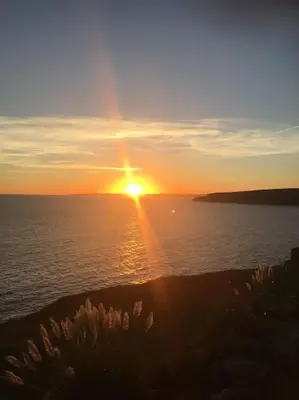 a sunset over a body of water with the sun at Wildly Romantic Cliff Top Apartment in Porthleven