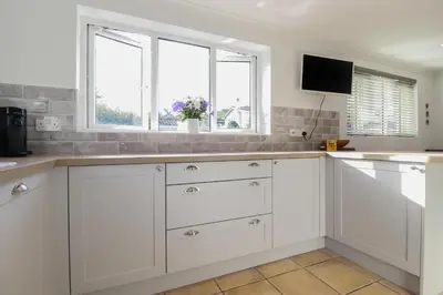 a white kitchen with white cabinets and windows at Surf Break in Wadebridge