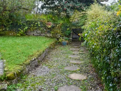 a garden with a gate and a stone path at Gew Cottage in Helston