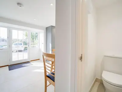 a white bathroom with a toilet and a chair at Starfish Cottage in Charlestown