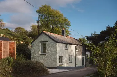 a small white house sitting on the side of a road at Topsy Turvy and Hillside Spa at Tregoose Old Mill in Newquay