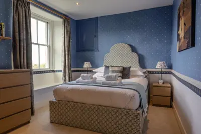 a bedroom with a bed with blue walls and a window at Trevornick Farm House in Newquay
