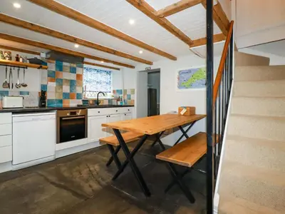 a kitchen with a wooden table and a staircase at Crab Cottage in Delabole