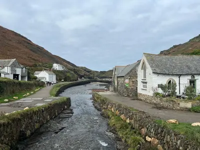a river in a village next to a stone wall at Rosebank Cottage in Boscastle