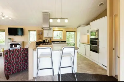 a kitchen with white cabinets and two bar stools at Cousins beach house Three bedroom lodge St Minver in Wadebridge