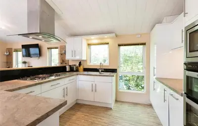 a large white kitchen with white cabinets and windows at Cousins beach house Three bedroom lodge St Minver in Wadebridge