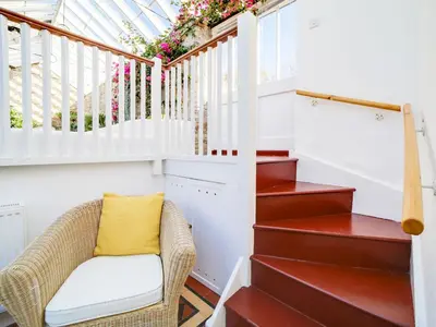 a wicker chair sits under the stairs in a house at Dolphin Cottage in Charlestown
