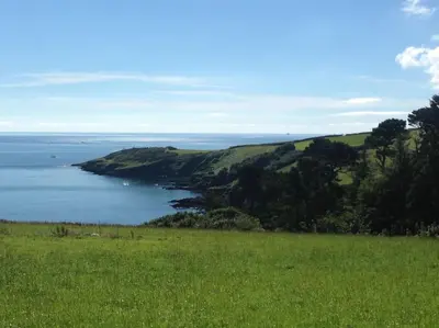 a green field with a view of a body of water at Little Bream - pretty cosy cottage, sea views, walk to the beach in Mawnan Smith