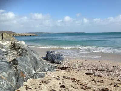 a beach with rocks and the water and the ocean at Little Bream - pretty cosy cottage, sea views, walk to the beach in Mawnan Smith