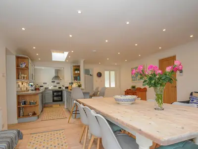 a kitchen and dining room with a wooden table and pink flowers at Seamay in Wadebridge