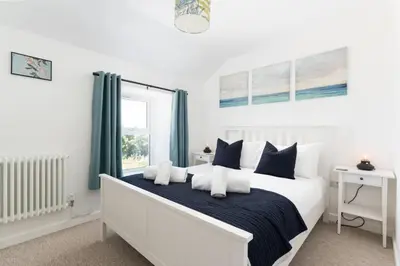 a white bedroom with a bed with blue and white pillows at Gwel Porth - St Ives - Sea Views in St Ives